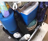 Top view of the cooler, foam sleeping pad, sleeping bag, folded map, and water bottles packed inside a black storage bin.