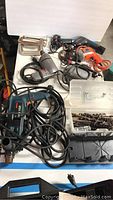 Overview of the lot showing multiple power drills including Bosch and Craftsman models, a plastic case with drill bits, clamps, and cords scattered on a white table.