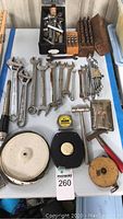Photo showing various sizes of metal wrenches laid out flat, socket wrenches, socket bits in holders, tape measures, and a hammer.