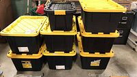 Stack of seven 27 gallon black plastic totes with yellow lids, two stacks visible, held securely together for storage and transport.