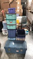 Stacked mixed color plastic storage totes including some without lids and a large chest-style tote