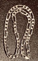 Full view of coiled sterling silver Figaro link chain necklace against a black background, showing overall length and clasp.