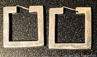 Front view of the pair of square sterling silver hoop earrings on a dark surface.