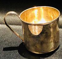 Side view showing overall shape and patina of the silver mug with handle visible.