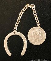 Front view of sterling silver horseshoe connected by chain to round saint medal showing saint figure.