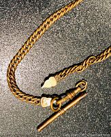 Close-up of entire length of a gold filled vintage pocket watch chain showing clasp and decorative elements.