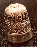Close-up photo of antique silver thimble showing textured floral pattern and engraved number 17 and name 'DREENA 1685' on band.