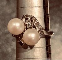 Angled top view showing two off-white cultured pearls and central round diamond, mounted on white gold gallery.