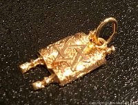 Close-up of 14 karat gold Torah pendant charm on a black surface, showing textured scroll and raised Star of David.