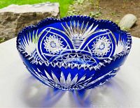Oblique angled view of the blue cut crystal glass bowl on a white surface outdoors, showing detailed cut star and fan patterns and scalloped rim.