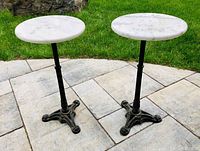 Full view of the pair of vintage round marble top side tables with cast iron bases on stone patio.