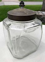 Full side view of the clear glass jar showing the embossed rib pattern and silverplate lid with black decorative finial knob.