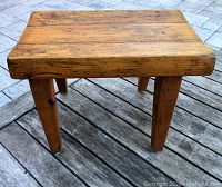 Front angled view showing top and legs of wood stool with worn finish and rustic character