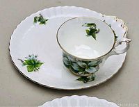 Pair of Royal Albert Trillium cups and oversized saucers showing floral pattern, gold trim, and scalloped edges.