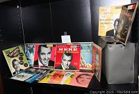 Photo showing a selection of Tony Martin 45 RPM records in original colorful sleeves and covers arranged in front of the original storage case.