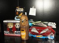 Photo showing Funko bobble head figures Luke Skywalker and Darth Vader, Dennys Chewbacca cup, Hot Wheels Star Destroyer vs Mon Calamari Cruiser die-cast vehicle in packaging.