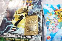 Gold textured Togepi collectible placed on a Pokemon Diamond & Pearl Secret Wonders card pack background, alongside a sealed Burger King 2000 Pokemon promotional toy/card in plastic bag.