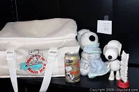 Full view of the five Snoopy collectible items including the insulated bag, root beer can, two plastic figures, and plush toy showing condition and scale