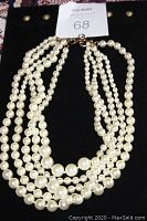 Multi-strand faux pearl necklace laid on black display highlighting graduated pearl sizes and gold-tone adjustable clasp.