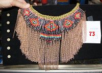 Close-up of the adjustable collar necklace held against black background showing beadwork and chain fringe detail.