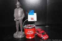 Photo showing the fireman statue, red fire bucket ashtray, and red fire department SUV toy together.