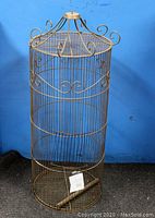 Full front view of vintage cylindrical metal birdcage with decorative scrollwork on top and midsection, showing oxidized brass patina.