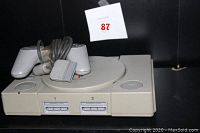 Front view of Sony PlayStation console with one gray controller placed on top, no cables visible.