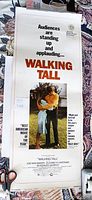 Photo of rolled movie theater lobby card for 1973 film "Walking Tall" showing main text and central embracing couple image.