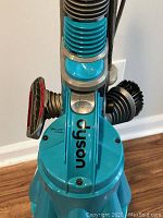 Top view of Dyson vacuum showing blue cyclone cone and hose attachment with cleaning brush