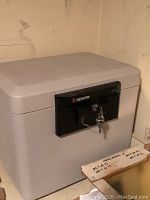 Closed light gray Sentry 1170 fire safe in corner with keys inserted into lock.