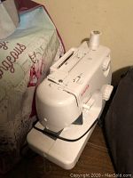 Front and left side view of Singer sewing machine showing spool of white thread, manual knobs and foot pedal cord.