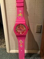 Front view of the Barbie wall clock shaped like a large pink wristwatch showing Barbie on the clock face and floral designs on the band.