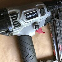 Side view of Husky pneumatic nailer showing handle, trigger, magazine, and Husky branding.