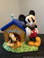 Front side showing Mickey Mouse leaning on the doghouse with Pluto inside and the blue bird on top