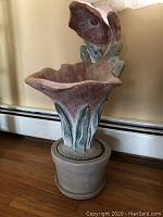 Front view of the ceramic plant planter shaped as a flower with bird/bud detail and round ceramic pot base on wooden floor.