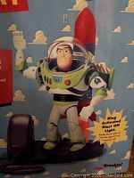 Photo showing boxed Buzz Lightyear phone with figure on base and rocket, highlighting the ring activated blast off light feature