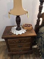 Photo of one pine nightstand with a lamp, small wooden box, and glass ashtray on top, showing drawer detail, wood grain, and wear on surface.
