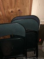 Photo showing three folding chairs stacked closely together, highlighting the backs with patterned fabric and black folding seats.