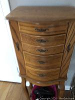 Front view of pine jewelry chest showing five curved front drawers and two side doors, featuring metal handles and sitting on carved legs.