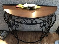 Front view of the demilune table showing the wood top and decorative metal base.