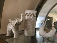 Elephant figurine, vase, and swan dish arranged in front of a mirror showcasing their features and glossy finish