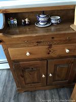 Front view of pine sideboard with drawer and two-door cabinet, decorated on top with ceramic and wooden figurines.