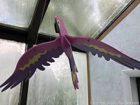 Wooden purple parrot decoration hanging from ceiling, shown from above and side angles