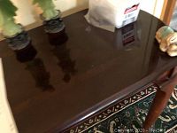 Close-up photo of the glossy cherry finish tabletop with orange reflections visible on the surface