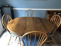 Full view of round oak dining table and four matching chairs arranged around it.