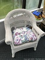 White wicker chair with floral cushion shown in close-up under sunlight, displaying detailed weave pattern and cushion design.