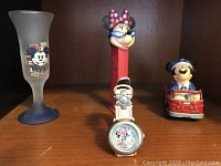 Full view of the lot showing Minnie Mouse Pez dispenser, Minnie Mouse watch, and Mickey Mouse shot glass on wooden shelf