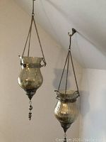 Both hanging vases shown suspended from ceiling hooks, showing their shapes, decorative metal parts, and chain supports.