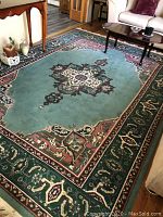 Full view of the green area rug with central medallion and patterned borders, placed in a living room with furniture around it.