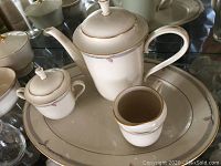Photo showing teapot, sugar bowl with lid, creamer, and serving tray with gold trim and floral accents in Lenox Gramercy pattern